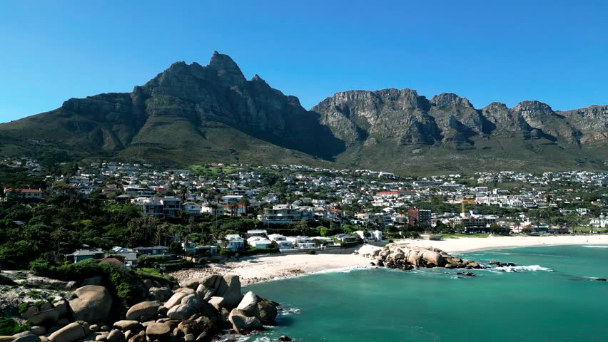 Aerial drone footage of Camps Bay beach in Cape Town South Africa with mountains in the distance showing coastal landscape and ocean scenery.