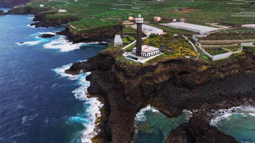 Aerial drone view of Punta Cumplida Lighthouse overlooking rugged volcanic coastline of La Palma in the Canary Islands, Spain. Dramatic cliffs, Atlantic Ocean waves, and coastal landscape captured from above in natural daylight.