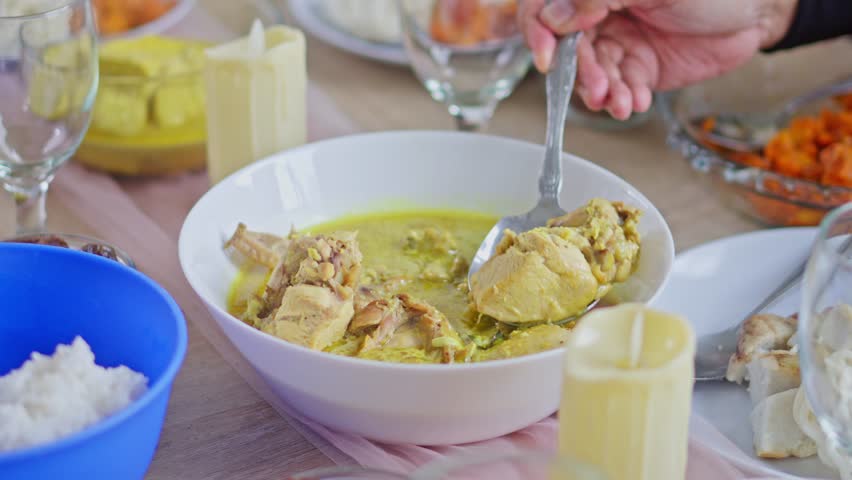 Close-up of Serving Indonesian chicken opor ayam into plate during an Eid al-Fitr family feast