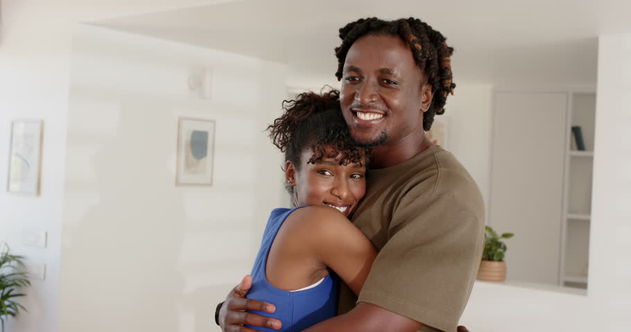 African couple posing, holding embrace at home in blue top and olive tee with framed art. Hug, affection, romance, connection, cozy, interior, living