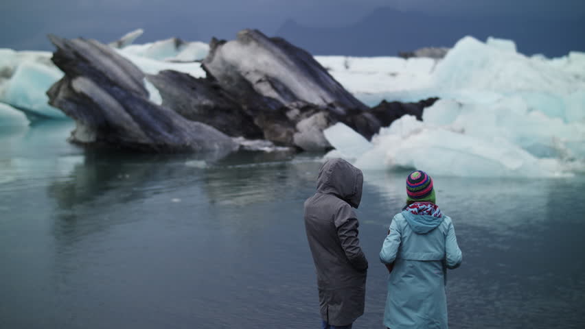 Two travelers watching drifting icebergs in Iceland glacier lagoon
