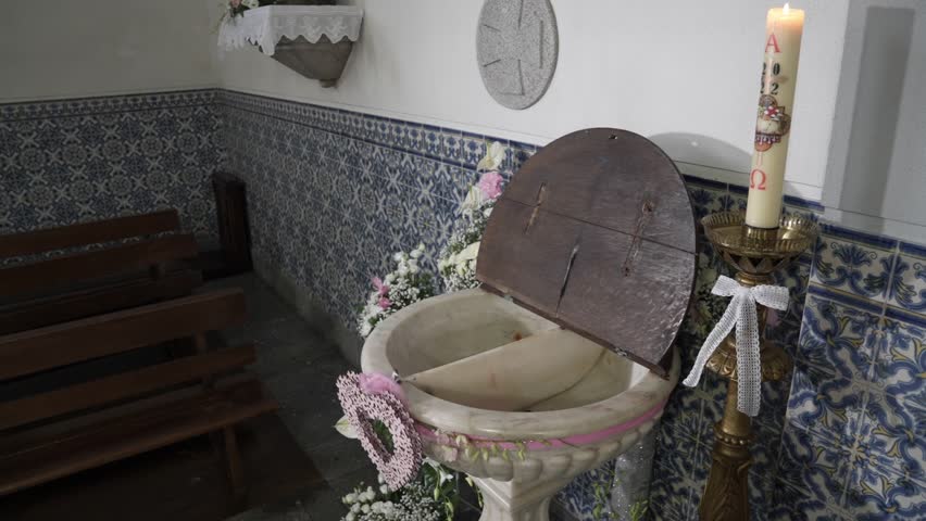 Baptismal font with open wooden lid candle floral decoration and tile walls