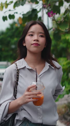 Young Asian woman strolling outdoors in the city while drinking a refreshing iced juice