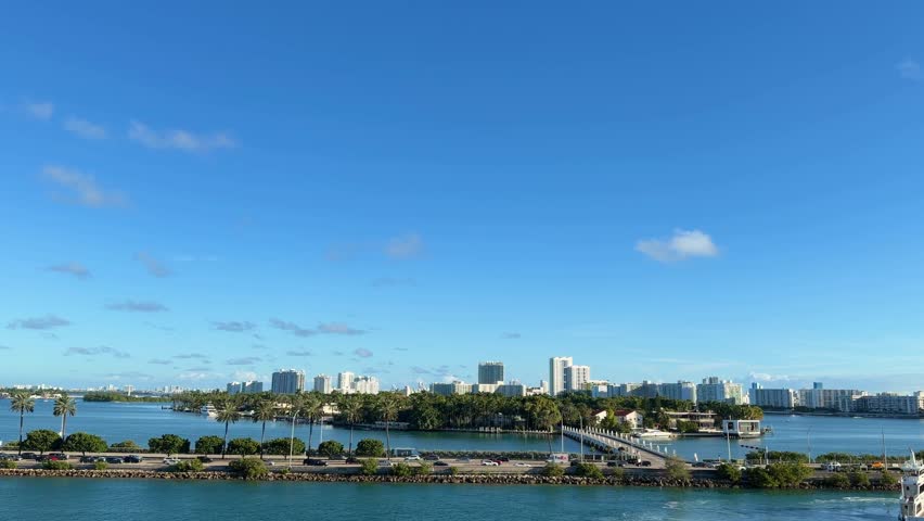 South Beach, Miami, Florida, showing a wide cityscape with modern buildings lining the waterfront, surrounded by lush palm trees under a clear blue sky creating a popular tourism destination view