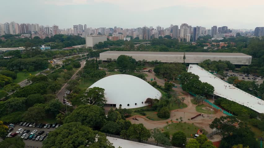 Aerial view pushing in, orbiting and tilting down toward Lucas Nogueira Garcez pavilion and Bienal pavilion at Ibirapuera Park in Sao Paulo, Brazil. Drone shot revealing Niemeyer architecture and modern structures