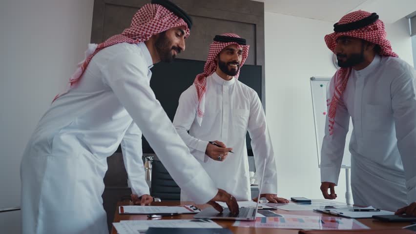 Arab businessmen wearing emirati kandura meeting in office for business deal - Corporate business group of middle-eastern people working in an international company in middle east
