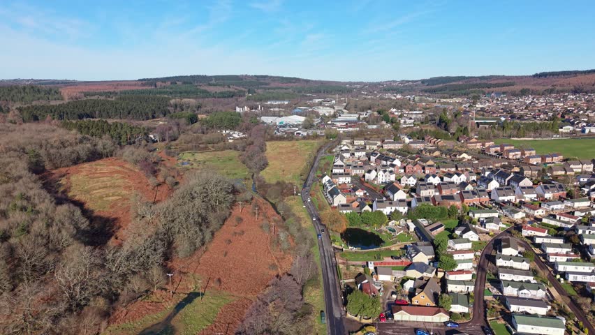 Drone aerial footage of Cinderford town in Gloucestershire, surrounded by the Forest of Dean, showing residential buildings, townscape, woodland, and rolling hills in a semi-urban rural English landscape.