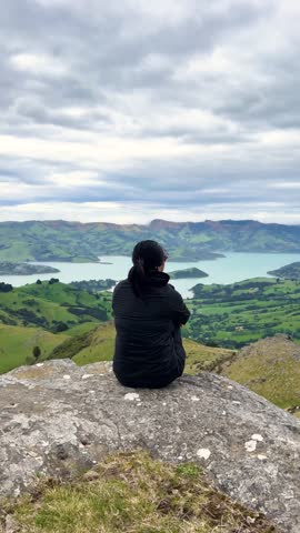 Asian woman views serene landscape from Montgomery Peak, Akaroa Peninsula, New Zealand
