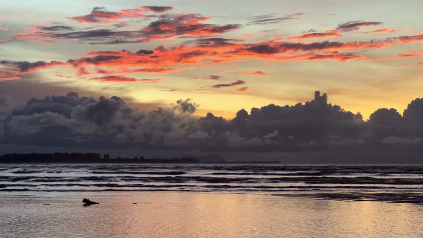 Vibrant tropical sunset over a calm ocean horizon with dramatic orange and yellow sky reflections on the water surface at low tide.