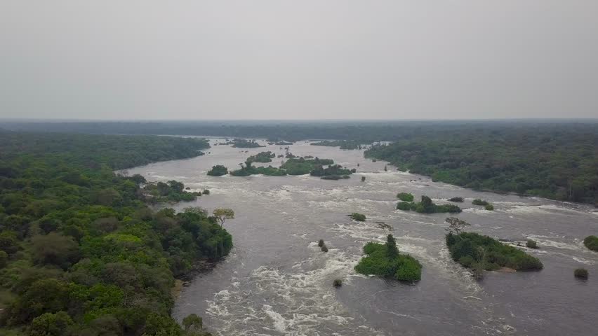 Nile River in Uganda flowing through Murchison Falls National Park, showing whitewater rapids, scattered green islands, and dense tropical forest stretching to the horizon, drone pand and reveal.