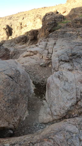 Cinematic view of the ancient, rocky terrain of the Hijaz mountains. the desolate beauty of a desert canyon floor with dramatic stone formations and sparse vegetation under a clear sky.