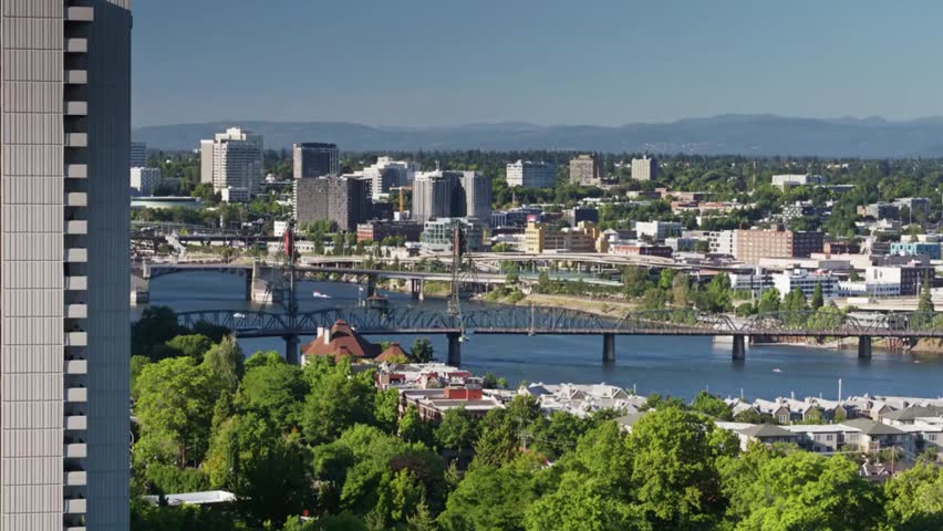 Aerial view of Portland, Oregon cityscape on a sunny day featuring downtown skyline, Willamette River, and scenic Pacific Northwest landscape.