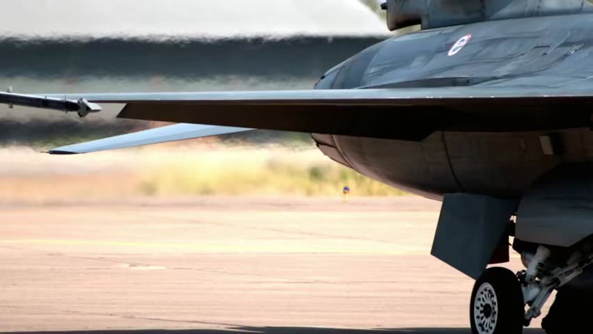 Close-up view of an F-16 Fighting Falcon on the tarmac, highlighting wing, landing gear, and military jet details under bright daylight.