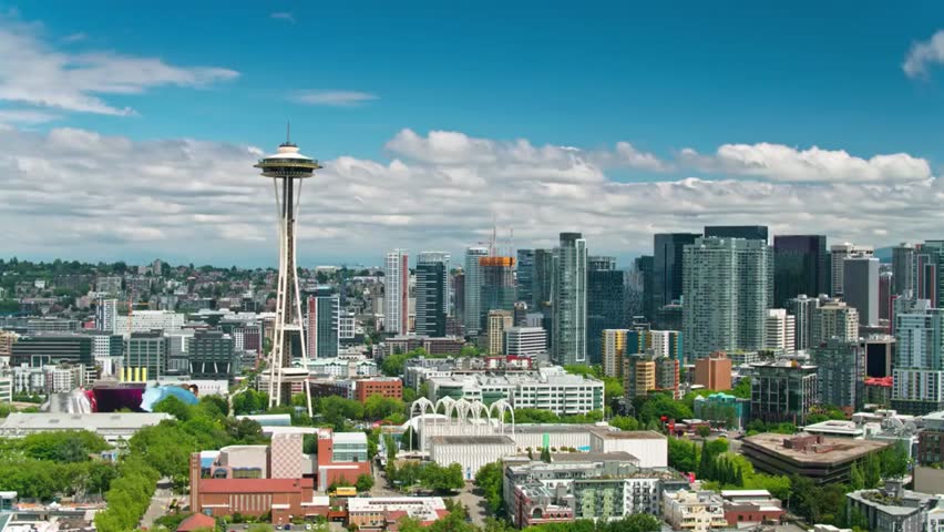 Aerial view of Seattle skyline featuring the iconic Space Needle towering over downtown under a bright blue sky with clouds.