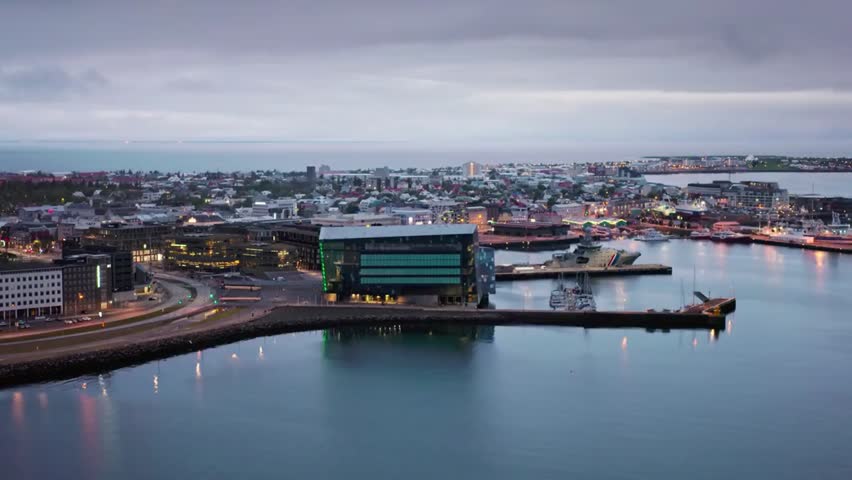 Aerial view of Reykjavik cityscape and harbor at dusk, showcasing colorful buildings, calm waters, and the scenic Iceland coastline.