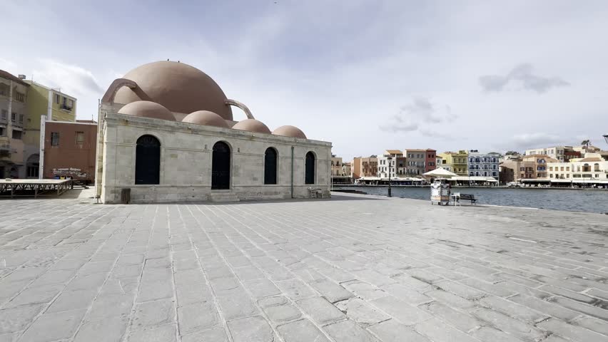 Slow cinematic view towards Küçük Hasan Mosque and iconic waterfront of the Old Venetian Harbour of Chania, with colourful facades and calm ocean waves [no people]