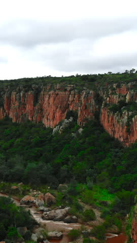 bold sandstone cliffs under cloud cover, majestic weathered stones amid lush greenery and arid stream