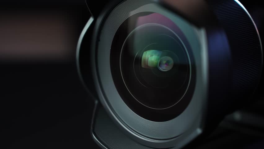 Macro close-up of camera lens as aperture blades move during power-on, with colorful glass reflections and cinematic shallow depth of field in a dark studio.