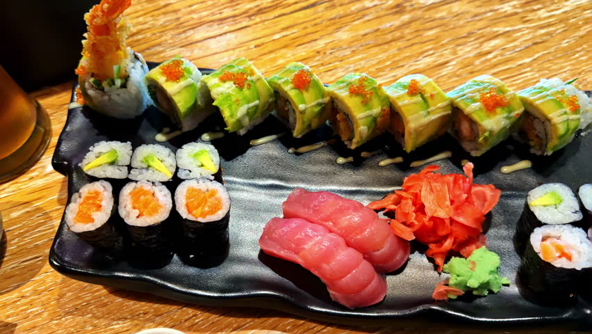 Close up footage of a sushi platter featuring assorted nigiri, maki, and specialty rolls with tuna, salmon, avocado, and roe. The presentation highlights variety, color, and Japanese dining.