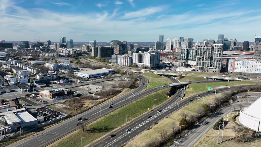 Establishing drone shot of Nashville skyline with highways and city streets near Fort Negley, modern towers under clear blue sky with bright sunlight and light traffic. Wide shot.