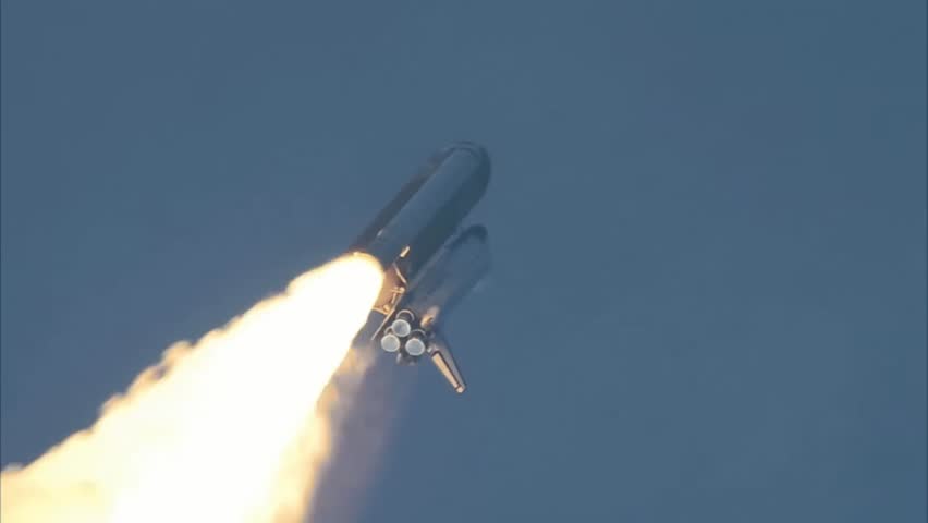 Space Shuttle ascending through the blue sky with bright exhaust flames.
