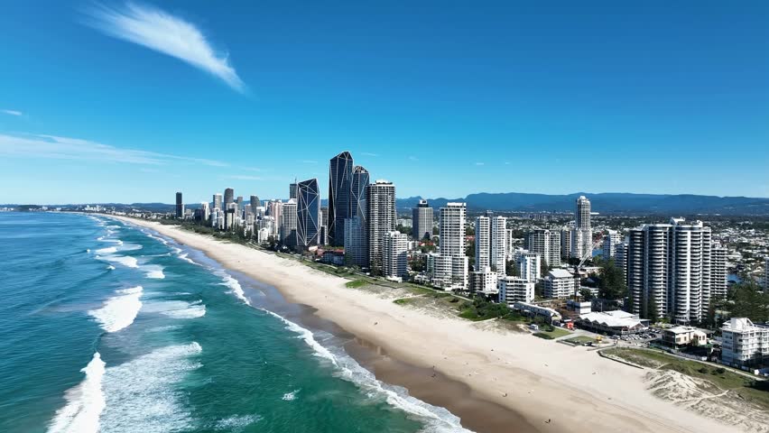 A drone glides above the stunning Gold Coast beaches, capturing shimmering turquoise waves, golden sands, and surfers enjoying a perfect summer’s day beneath the bright Aussie sun.