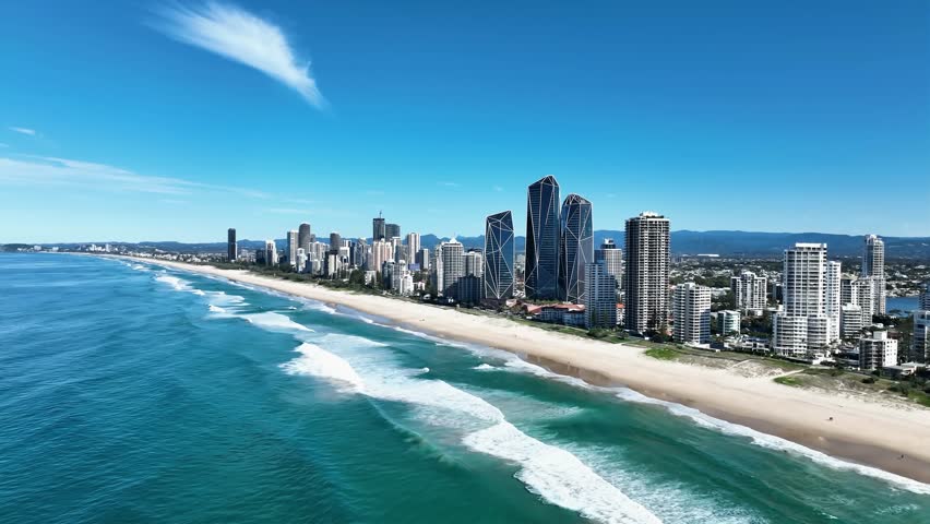 A stunning aerial view of the suburb of Main Beach on a sunny day, captured from a drone flying south, showcasing golden sands, blue ocean waves, and a vibrant coastline. Iconic Queensland