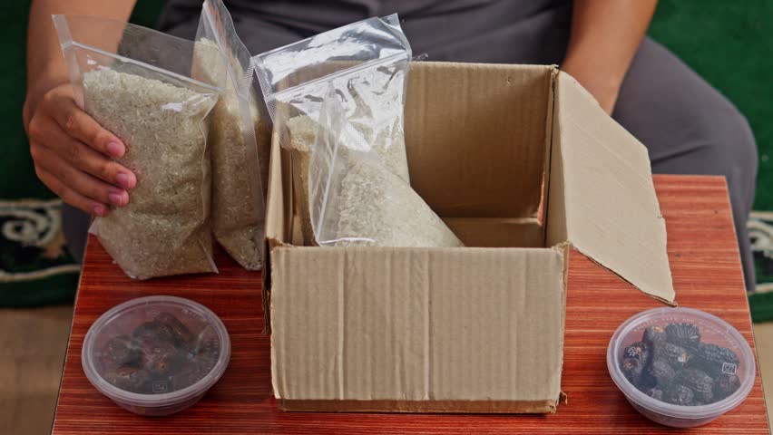 Hands placing plastic bags of raw rice into box for zakat al-fitr distribution