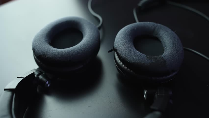 Close-up of worn over-ear headphone ear pads on a dark desk with soft studio light and shallow depth of field, ideal for audio gear, music production, and tech b-roll.
