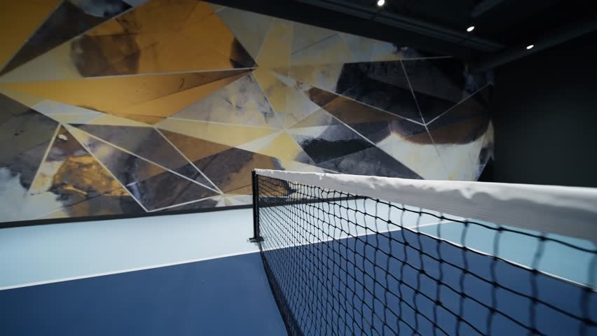 Indoor pickleball net with modern court design and abstract mural wall, camera slowly pulling back