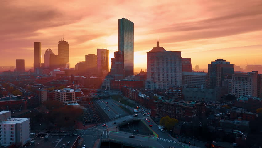 Pink-orange sky over the cityscape of Boston, Massachusetts, USA. Drone footage above the lively highways at sunset time.
