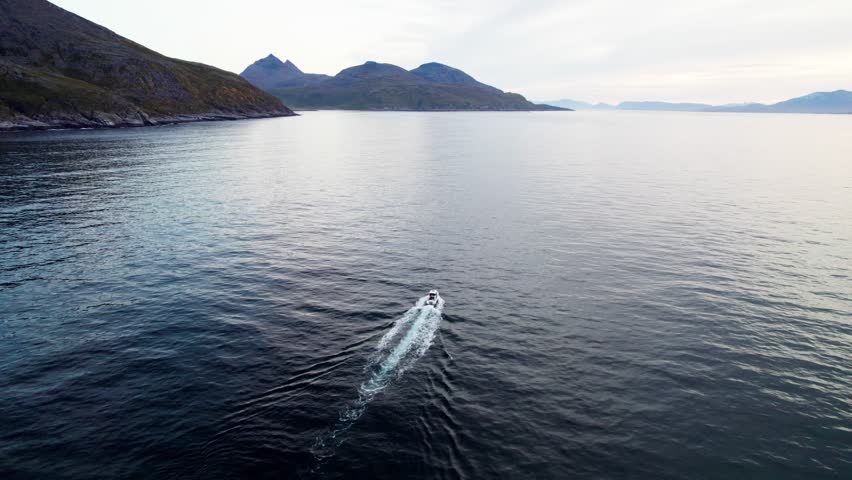 Aerial drone footage flying left to right following a moving fishing boat, mountains in the background, cinematic Nordic coastal landscape.