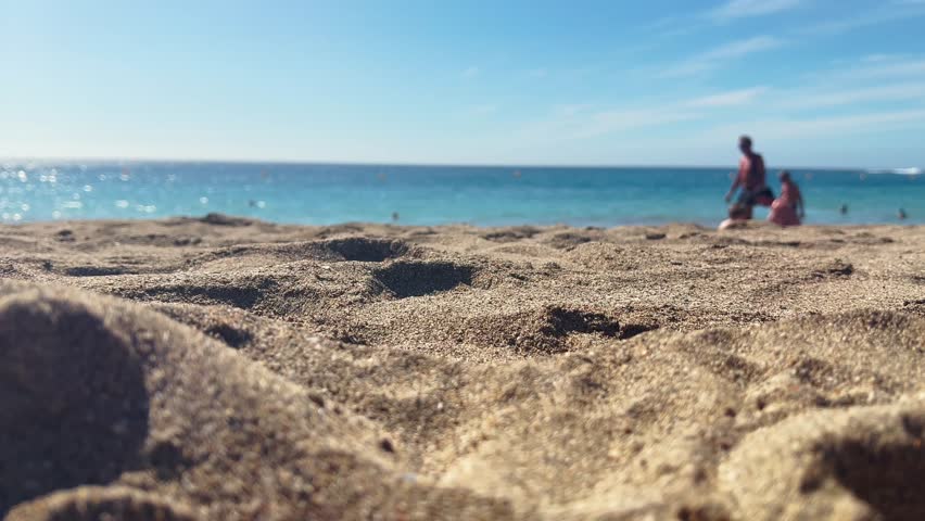 Close-up of sunlit sand on a beach in Tenerife with soft movement of unrecognizable people in the distant background.