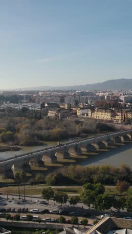 Vertical aerial view across the river highlighting the historic Roman Bridge in Córdoba, Spain.