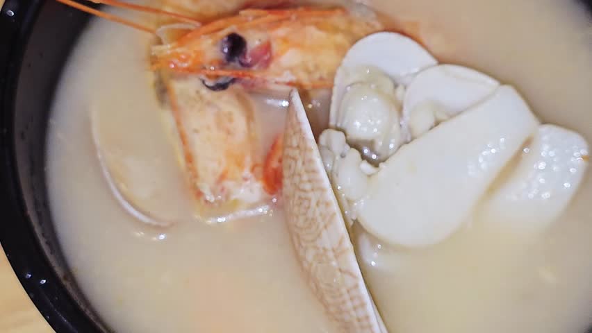 assorted seafood creamy soup of shrimps, squid, crabs, fish fillet, herbs, dill, garlic and onion, seafood mixture hot soup, healthy food concept of pieces of various sea food, selective focus