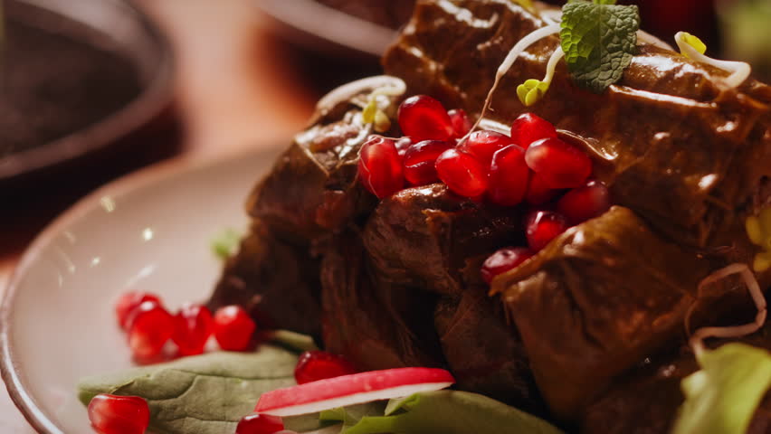 Close up of stuffed vine leaves topped with rich sauce and pomegranate seeds on plate.