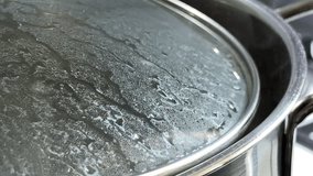 Water boils intensely inside a stainless steel pot covered with a glass lid. The trapped steam condenses into droplets as the water gurgles and splashes against the surface. - Powered by Shutterstock - Get 15% off with code: PIKWIZARD15
