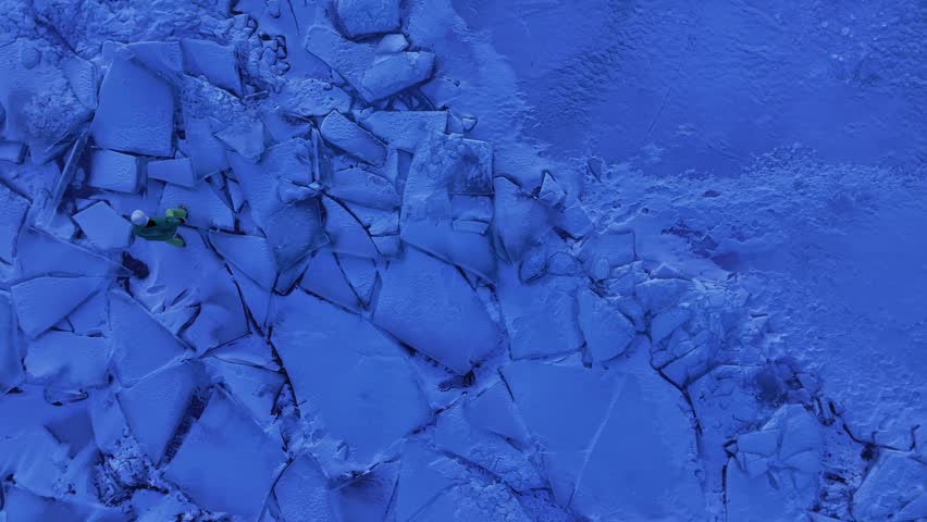Dramatic orbit shot around a person standing on jagged fractured ice sheets of a frozen lake during blue-hour twilight at Lake Baikal, Siberia, 4K aerial footage.