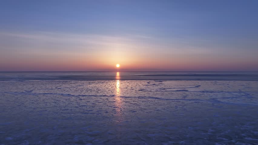 Static shot of a serene sunset over a frozen lake, revealing intricate crystalline ice patterns in 4K aerial footage at Lake Baikal, Siberia.