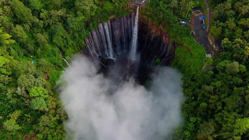 4K Top down aerial view of Tumpak Sewu waterfall basin in East Java, Indonesia. Dense jungle surrounds the circular canyon as mist rises from cascading water below.