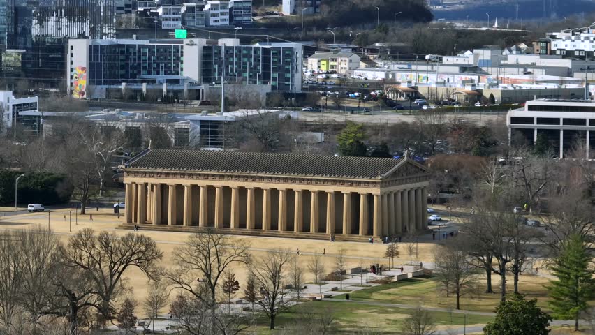 Aerial view of Parthenon in Nashville Tennessee, iconic Greek revival landmark in Centennial Park with city buildings in the background. Wide shot. Sunny day in America.