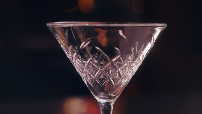 Close-up of a bartender pouring a pink sour cocktail with foam into a coupe glass in a stylish bar setting.