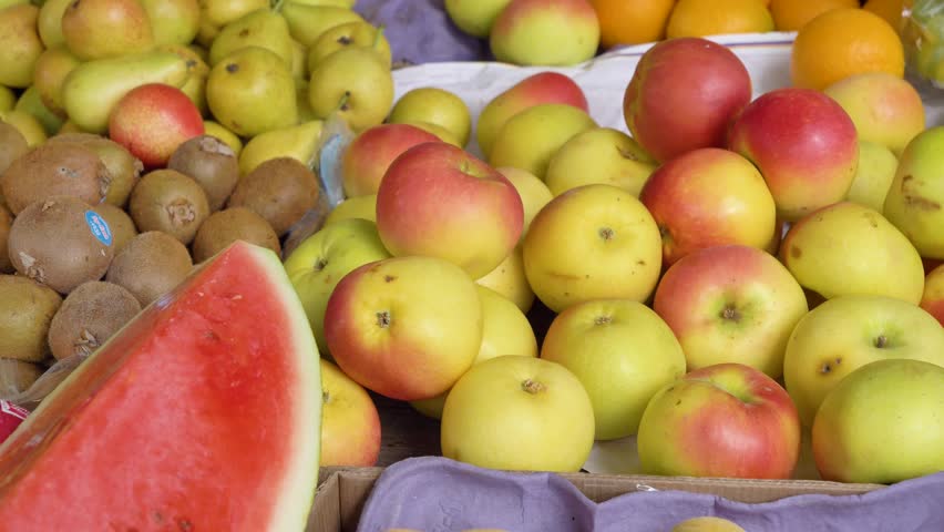 Close up view of apples, sliced watermelon and kiwi displayed on a local market stall.