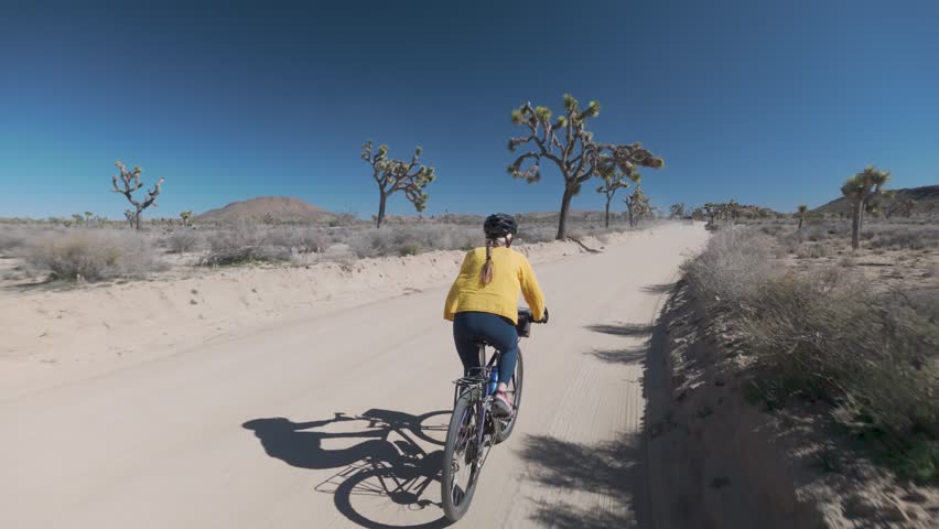 Mature woman rides her bike on a dirt road surrounded by desert rocks and Joshua trees in Joshua Tree National Park California