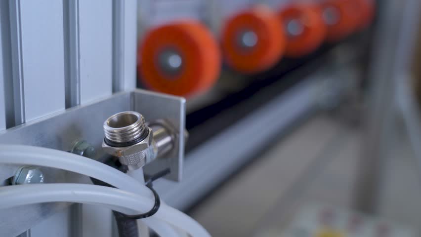 Close-up of a pneumatic fitting and hose on an automated industrial machine with orange rollers