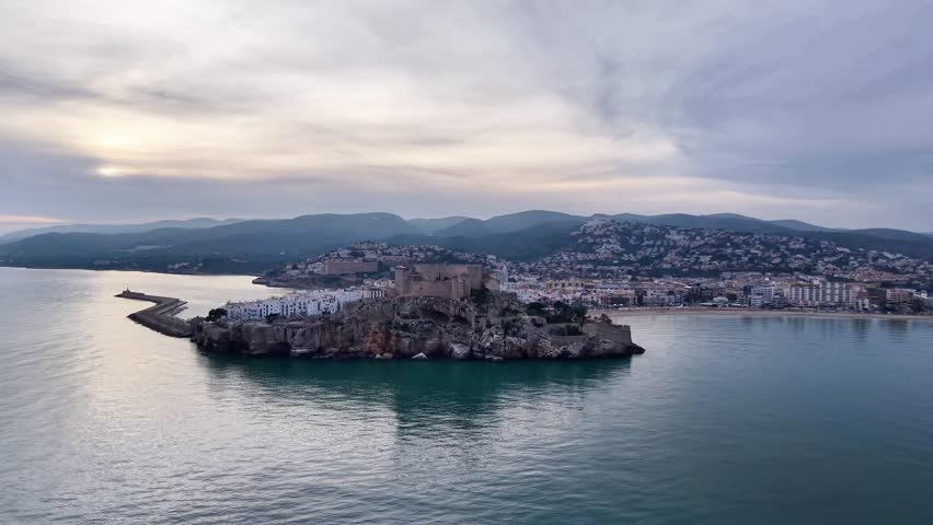 Historic coastal panorama. Castle reflections over tranquil waters. Serene sunset scene with ancient walls and reflective emerald waters
