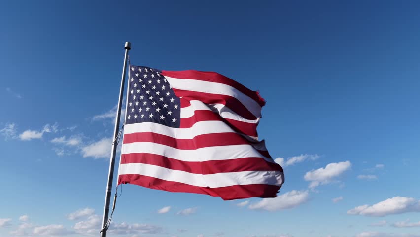 Waving patriotic American flag against blue sky and sunlight. Aerial close up view in USA. Proud and pride nation of United States. Stripes and stars in red blue and white color. Aerial view.