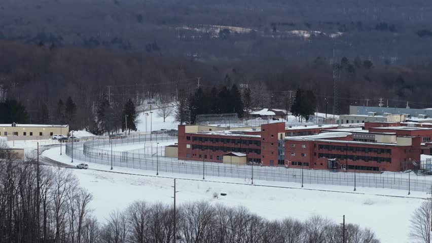 Aerial view of Federal Correctional Institution Loretto in Pennsylvania with perimeter fence, guard road and snow covered grounds in winter. Wide shot.