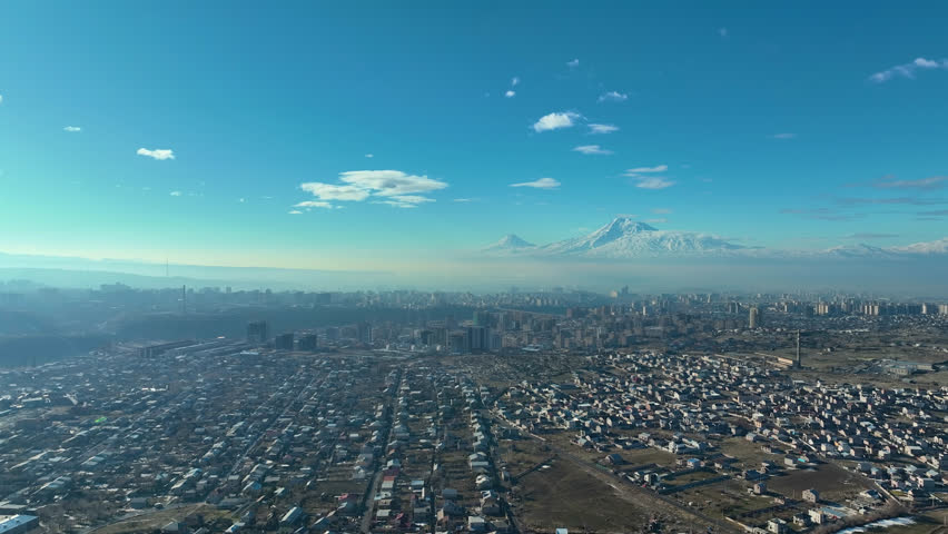 A city with a mountain in the background. The sky is clear and blue. The city is full of buildings and people