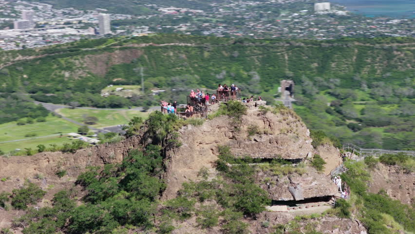 Aerial orbital shot of people on the top of Diamond Head Mountain overlooking Waikiki Beach and Honolulu city skyline, Hawaii
